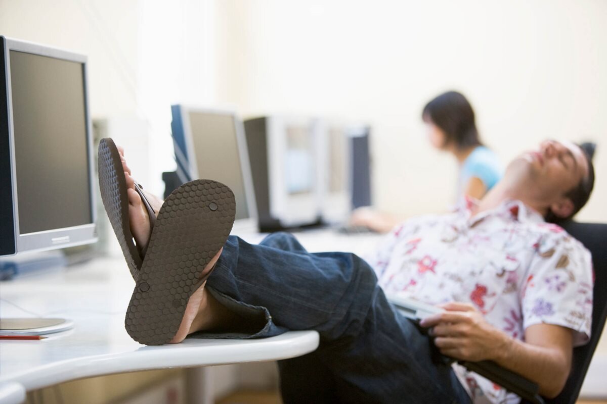 Someone sat in an office, laid back in their chair, with their feet on the desk, wearing sandles